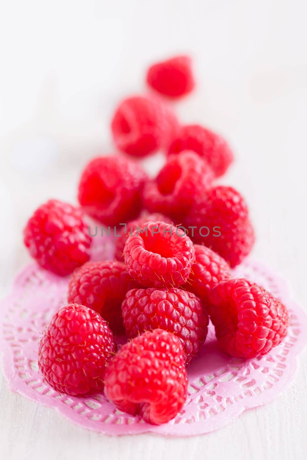 Closeup of bunch of fresh red raspberries resting on decorative pink mat on light surface