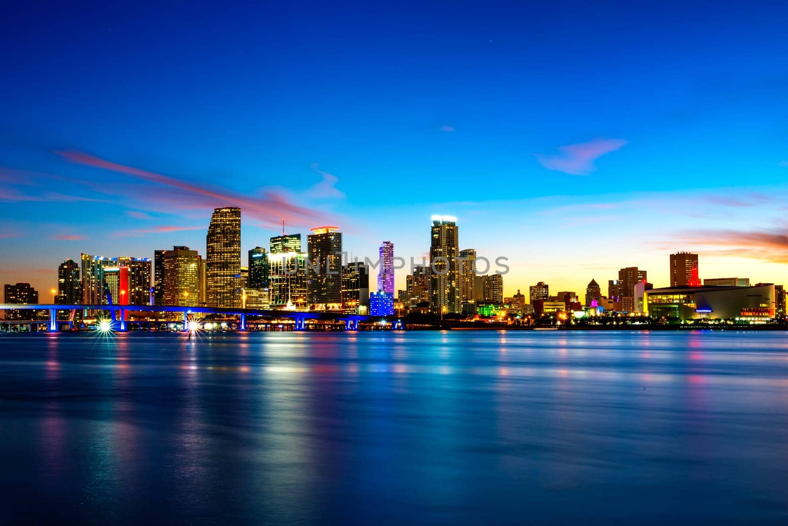 Miami city skyline panorama at dusk with urban skyscrapers over sea with reflection