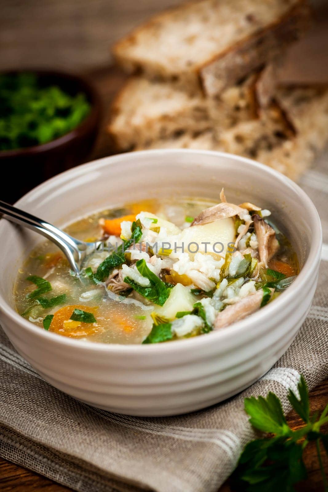 Chicken rice soup with vegetables in bowl and bread on rustic table