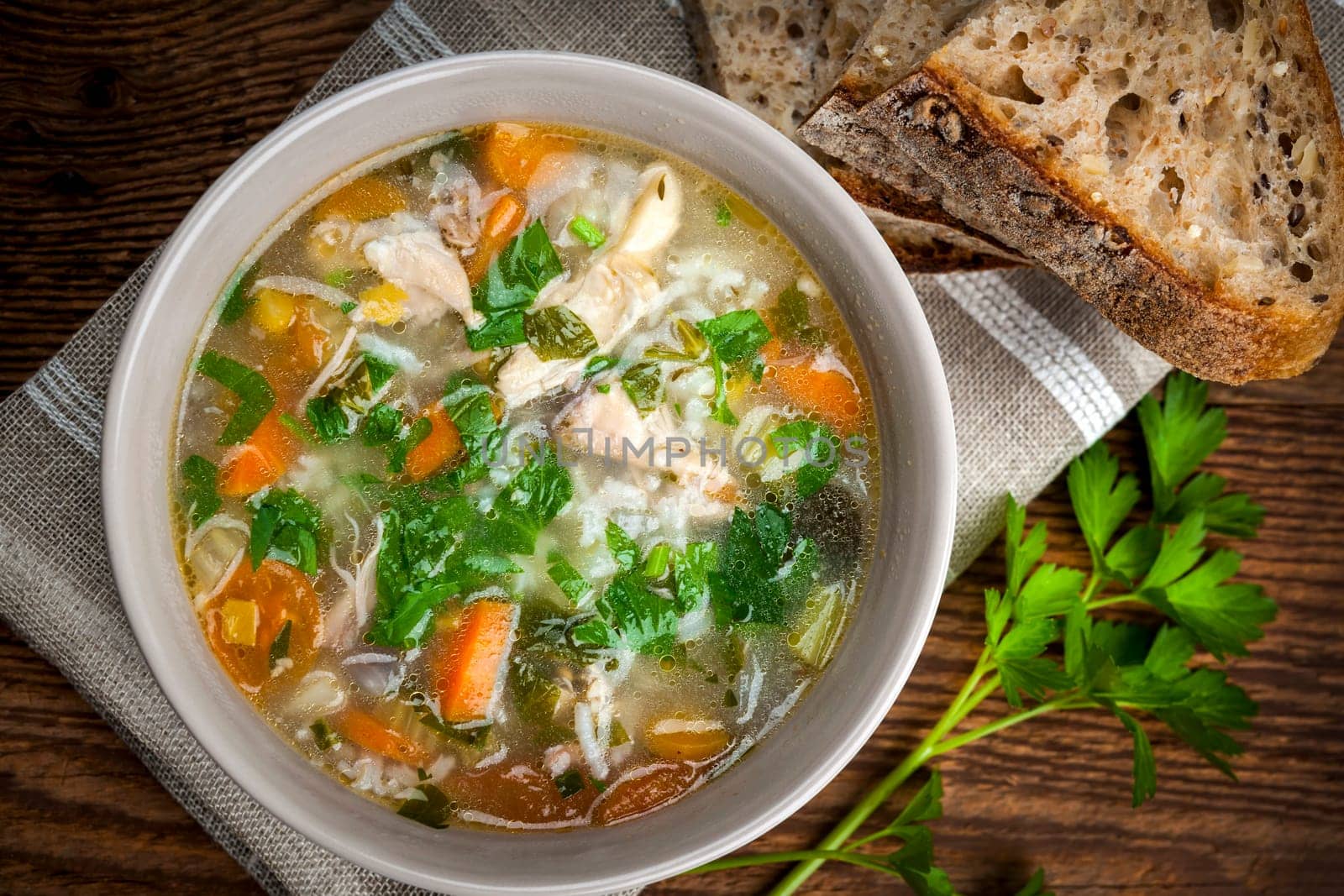 Chicken rice soup with vegetables in bowl and bread from above