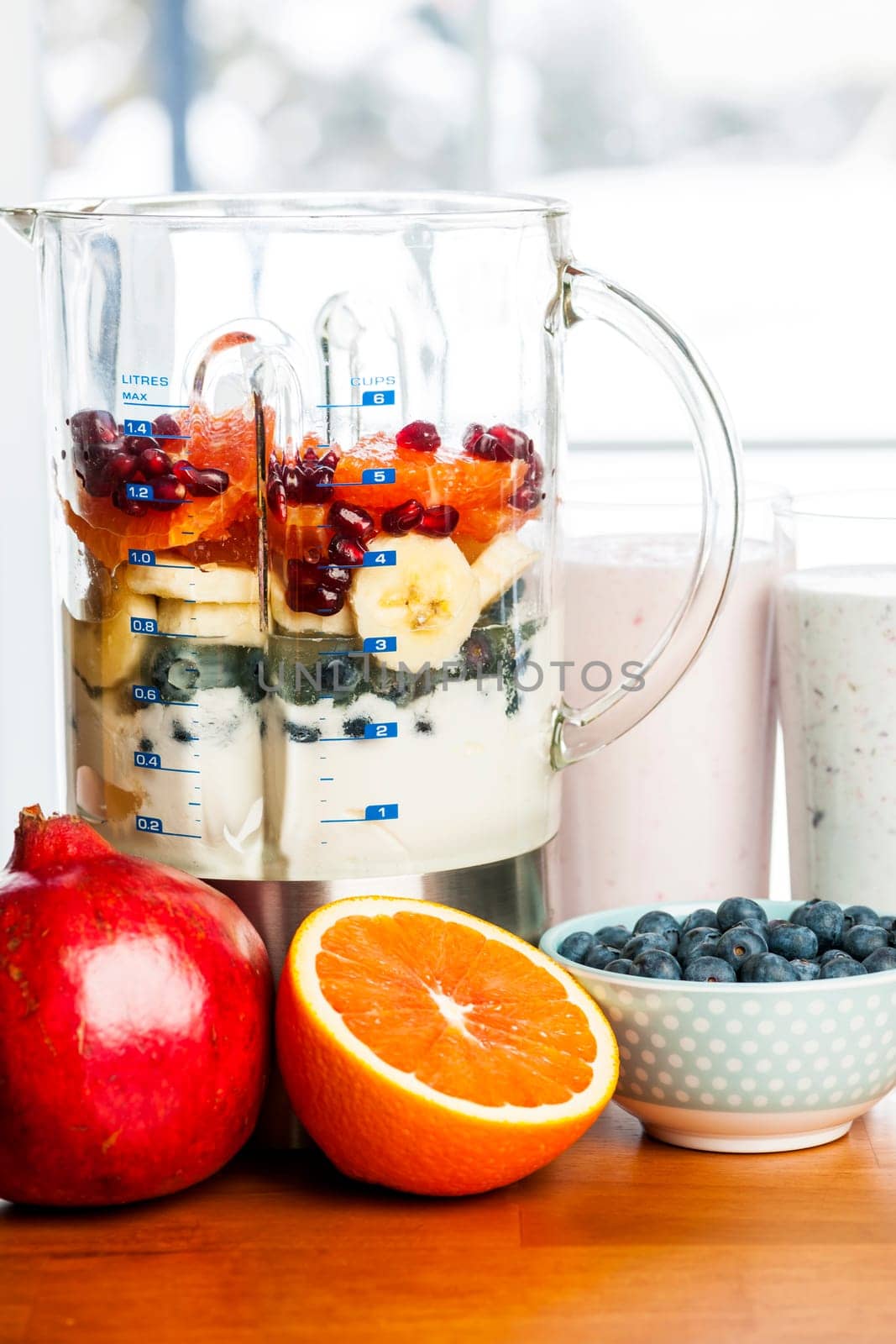 Prepared smoothies and healthy smoothie ingredients in blender with fresh fruit ready to blend on kitchen table