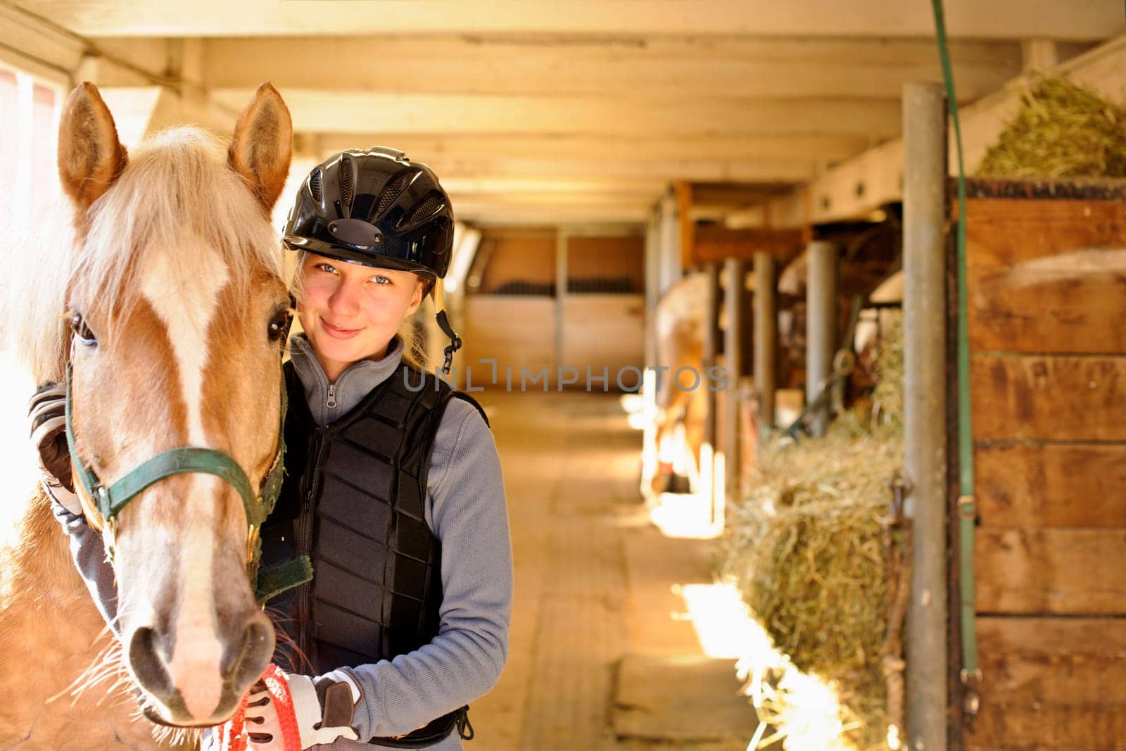 Young female rider with horse inside stable