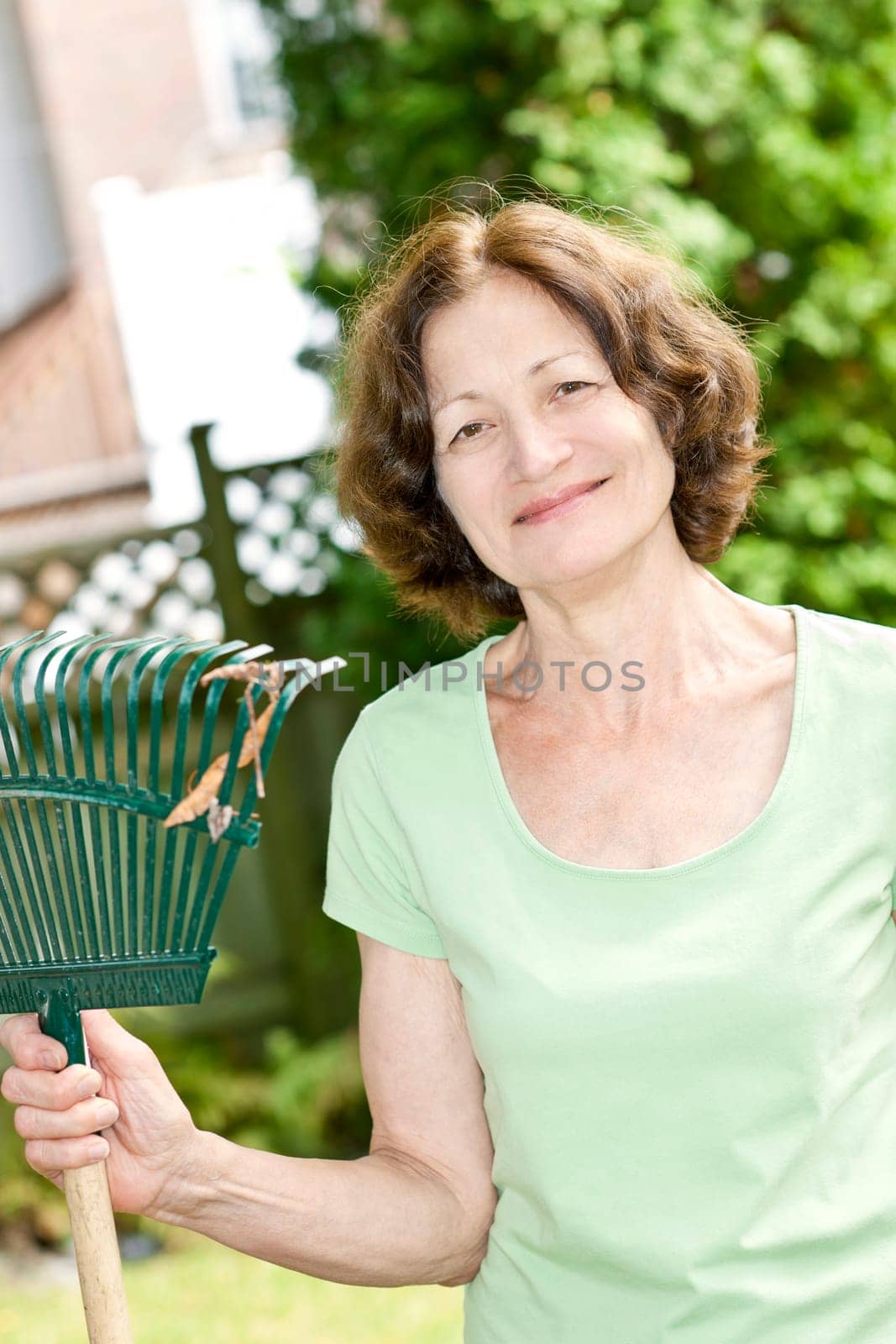Senior woman smiling holding rake and gardening outside