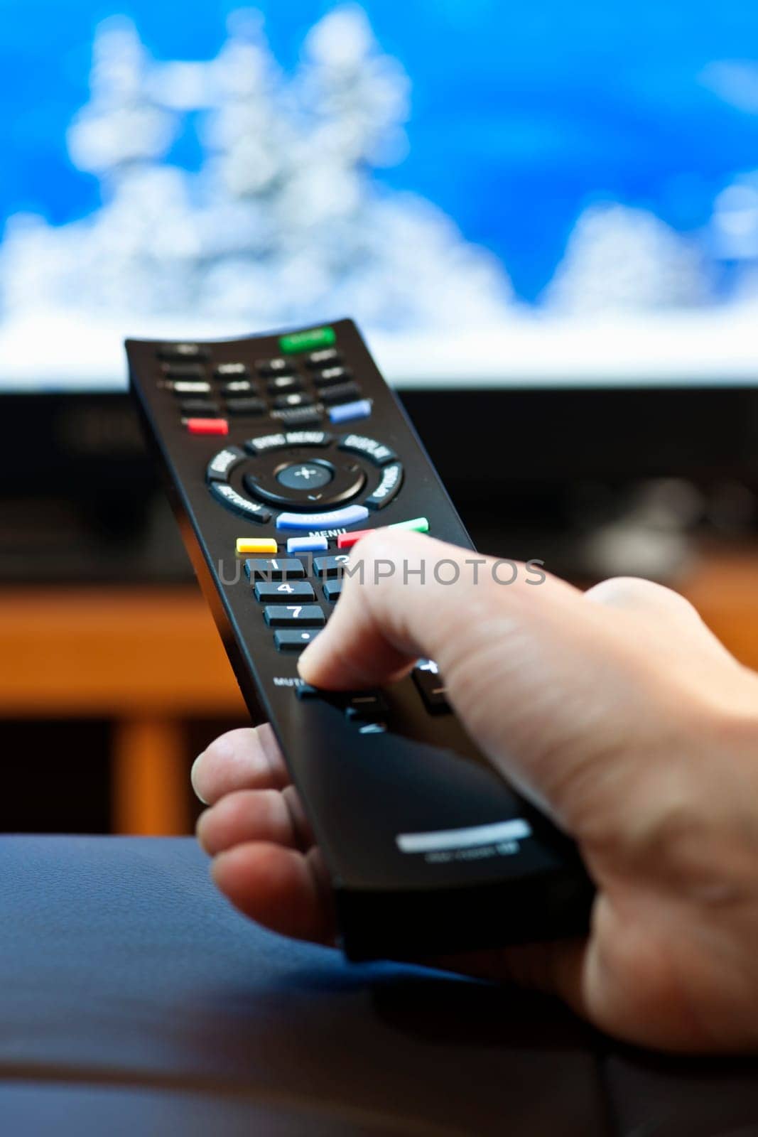 Hand holding television remote control pressing buttons