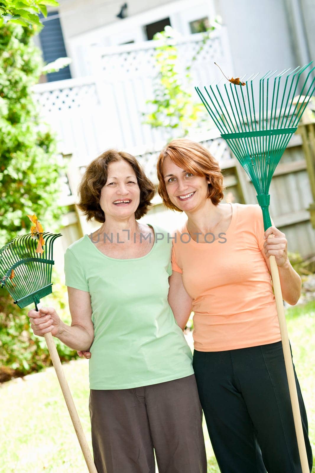 Mother and daughter holding rakes gardening outside