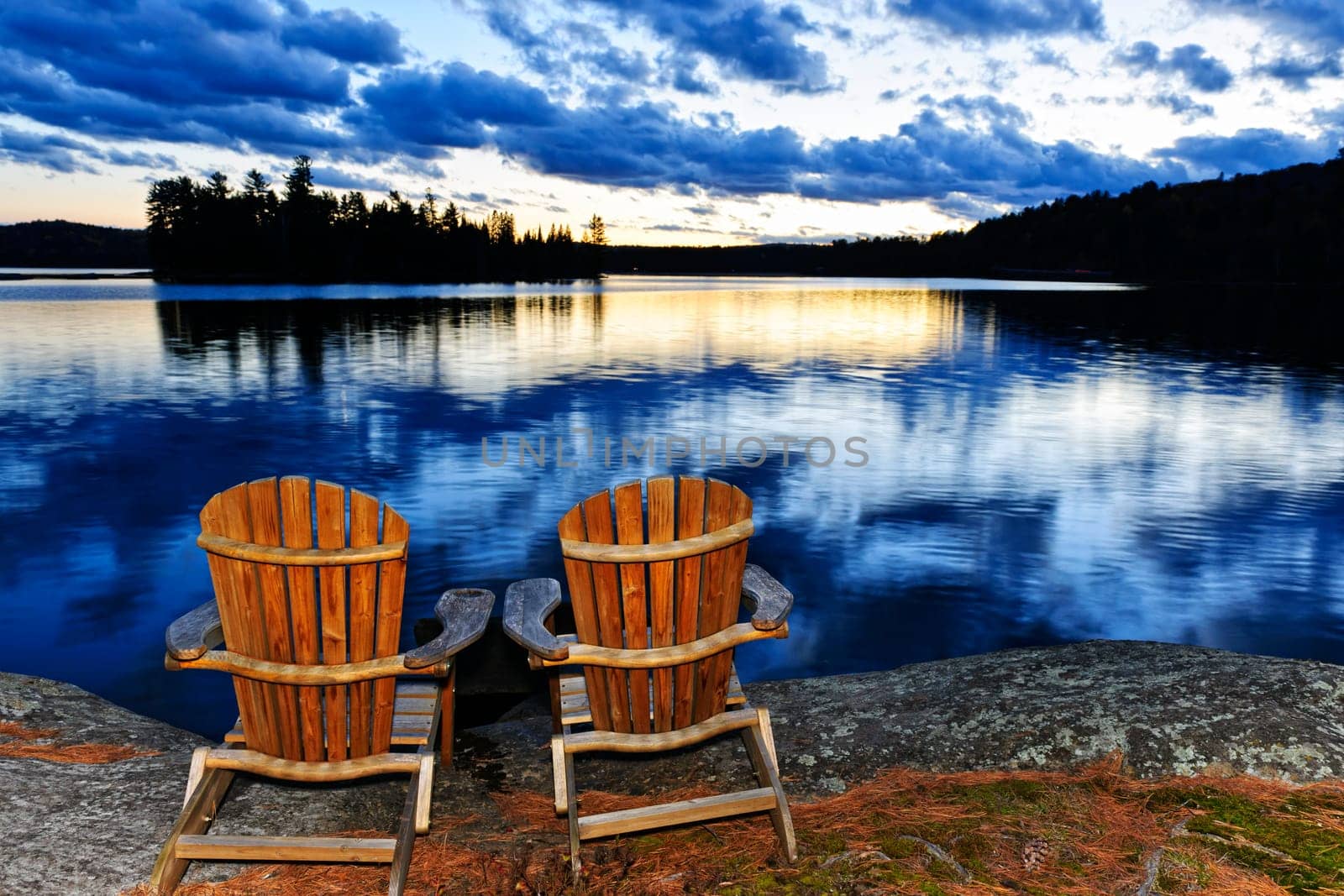 Landscape with adirondack chairs on shore of relaxing lake at sunset in Algonquin Park, Canada