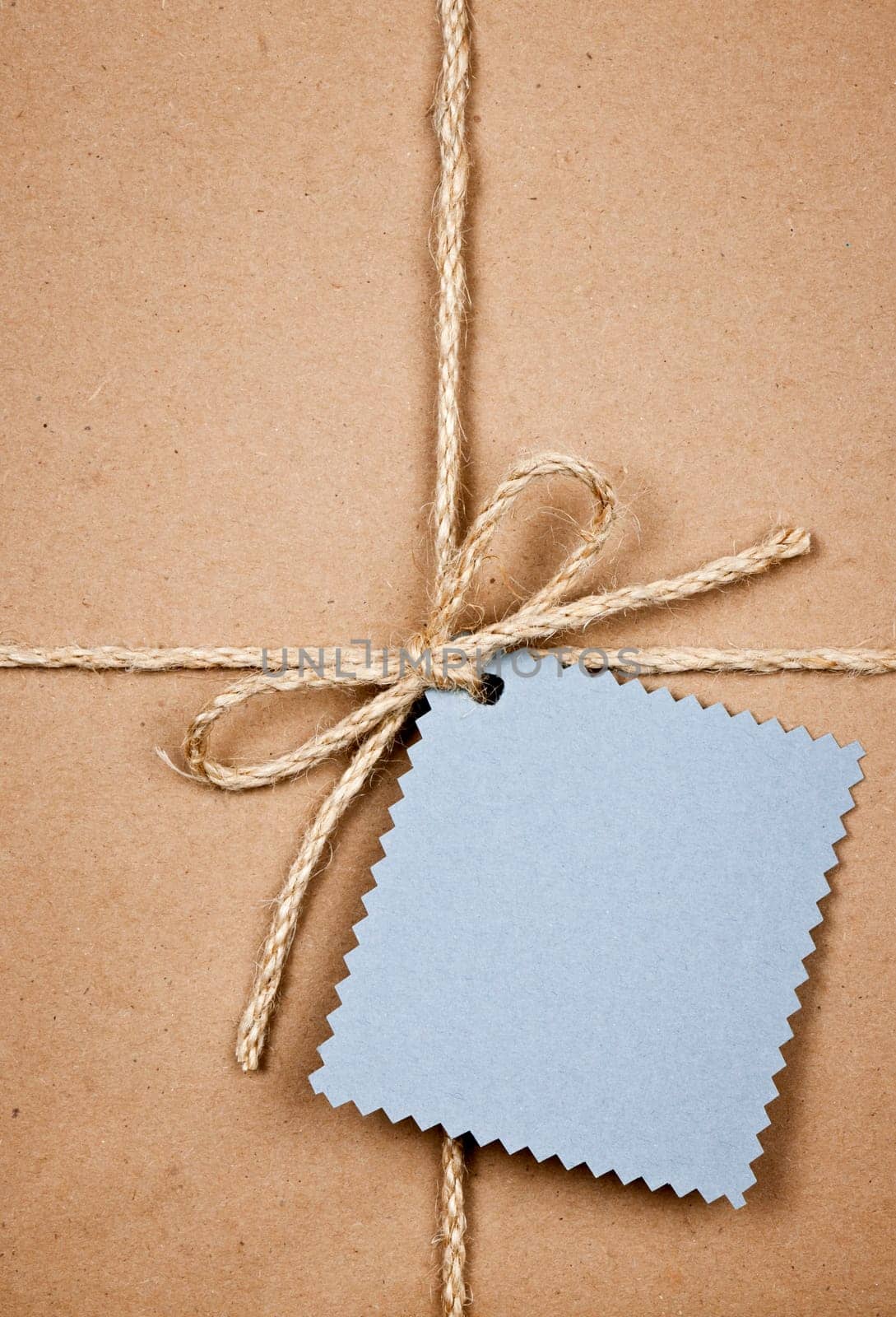 Gift package and blue tag in brown paper wrapper tied with string close up