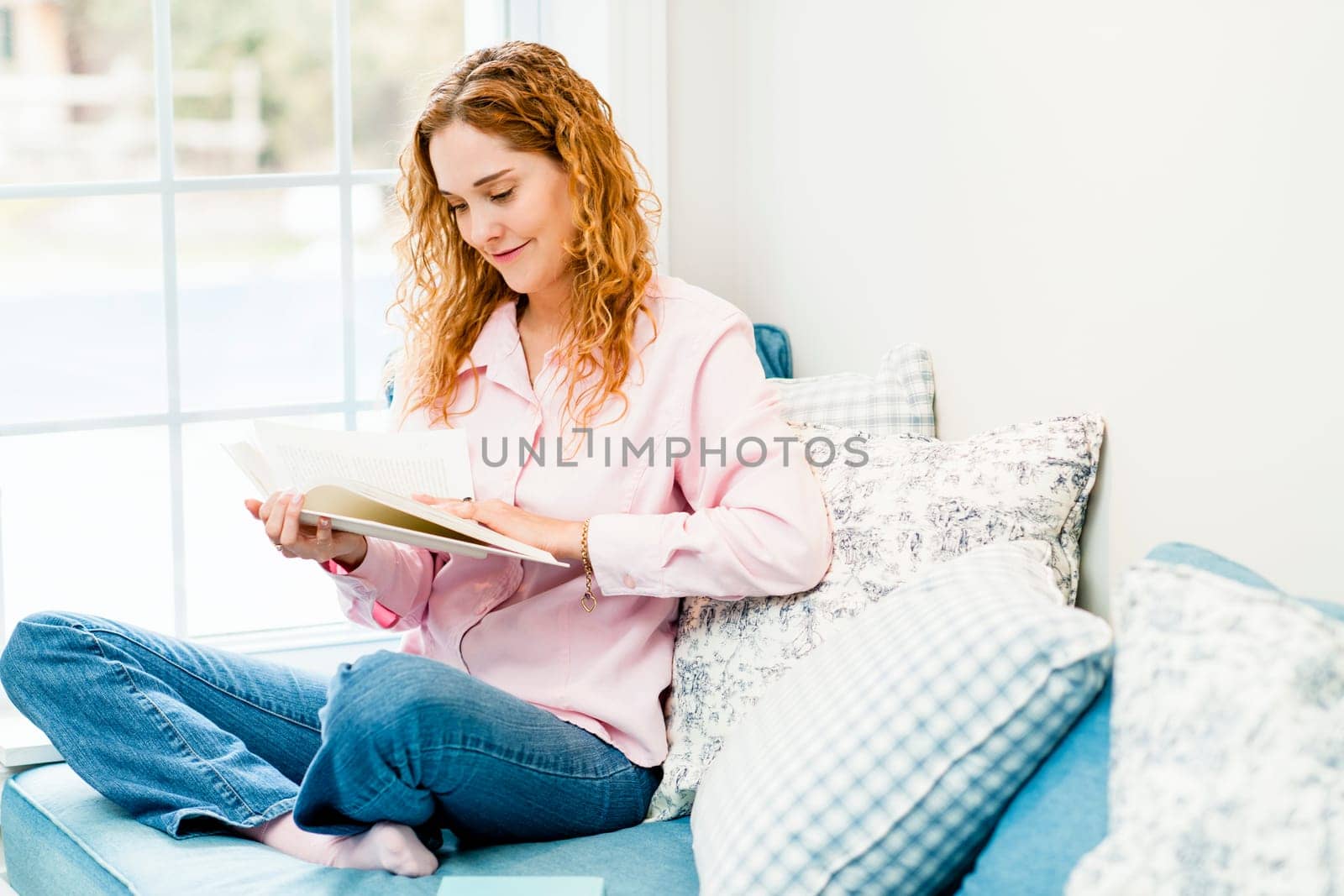 Smiling caucasian woman reading book by window at home