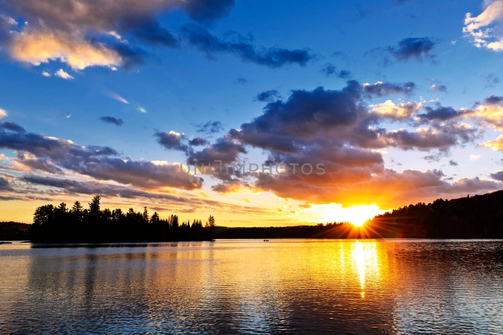 Sun setting over tranquil lake and forest in Algonquin Park, Canada