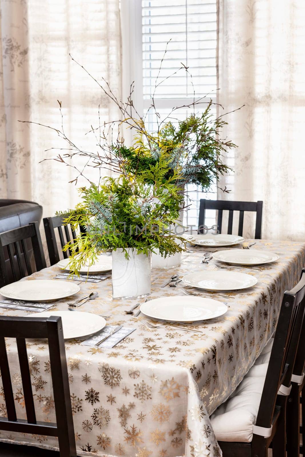 Dining table decorated for Christmas with eight place settings and evergreen centerpiece