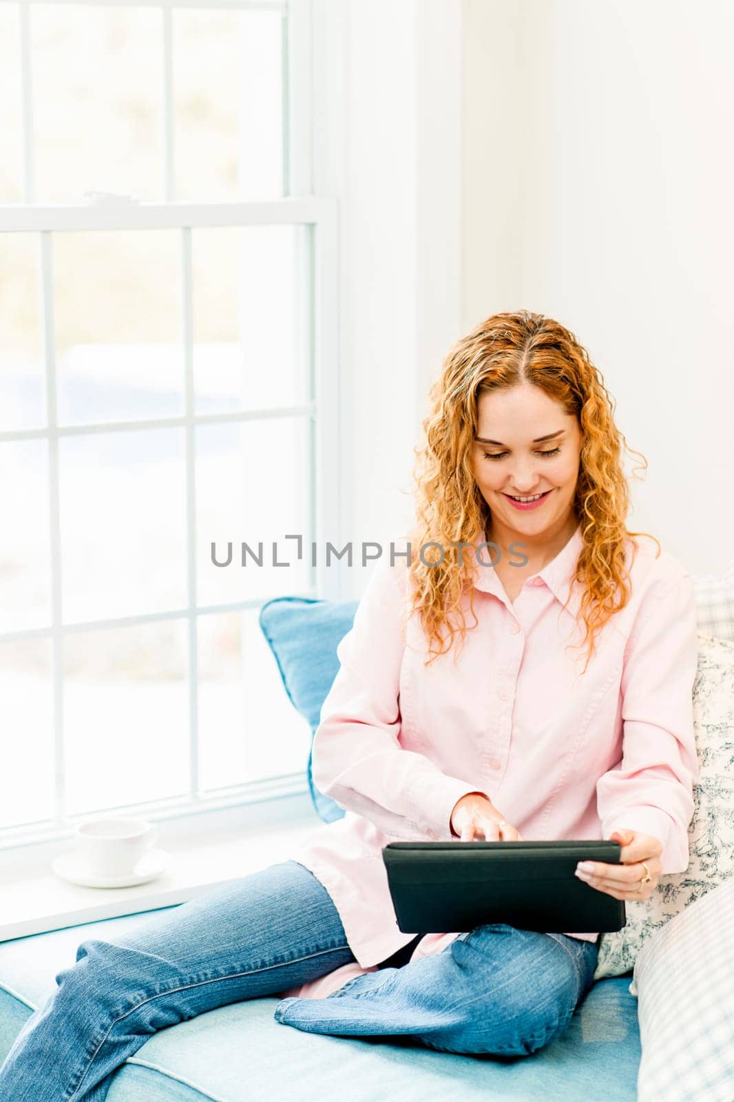 Smiling caucasian woman using tablet computer at home by window