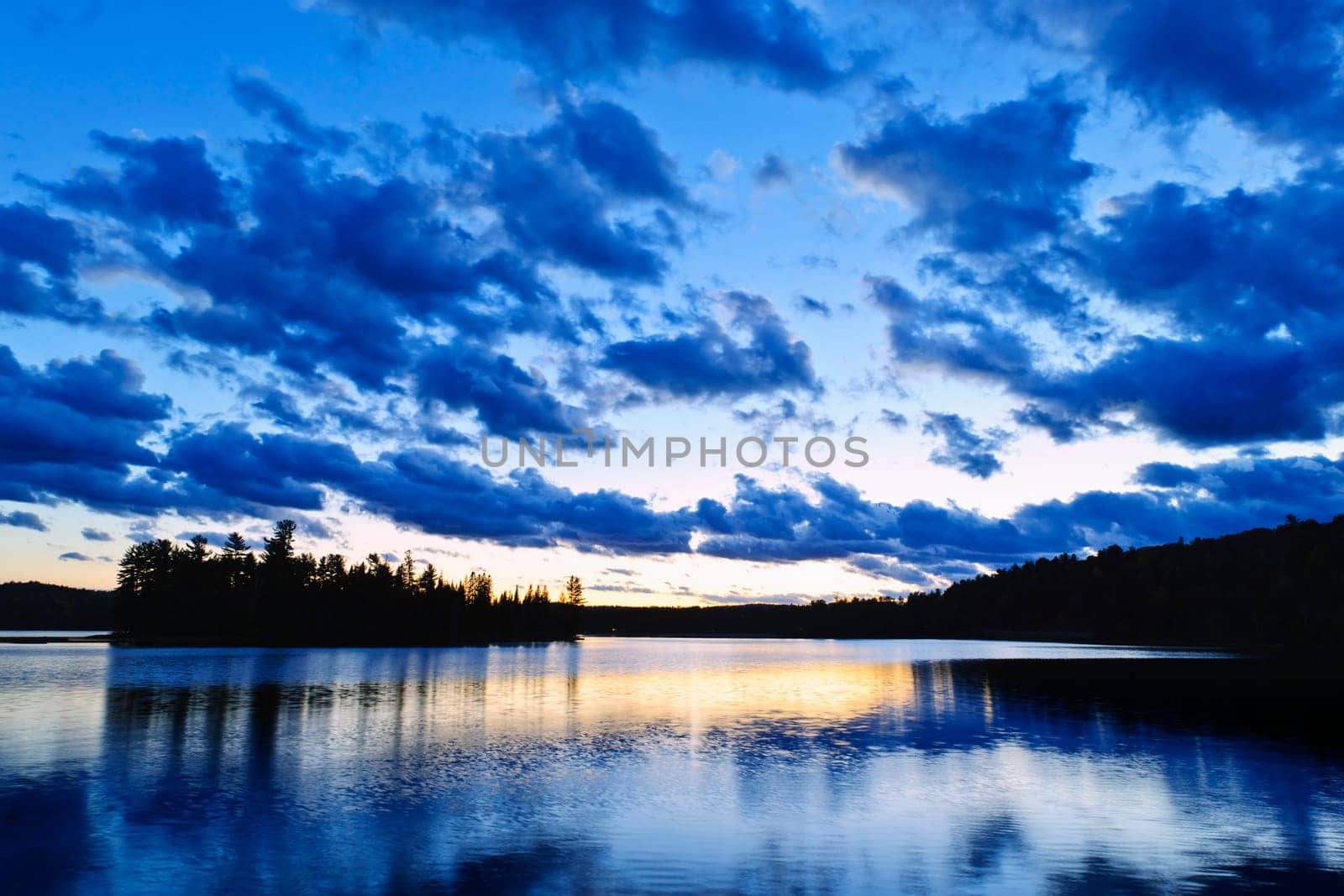 Sun setting over tranquil lake and forest in Algonquin Park, Canada