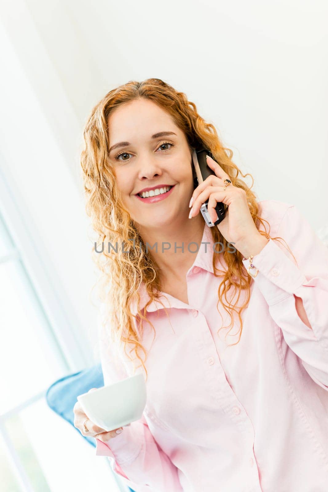 Smiling woman using cordless phone and drinking coffee