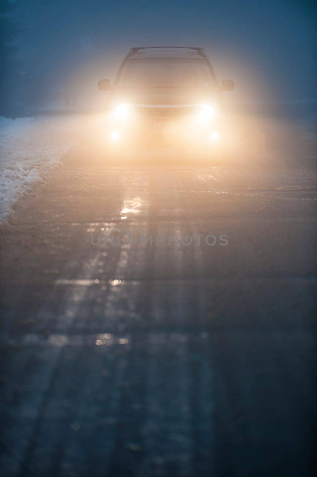 Bright headlights of a car driving on foggy winter road