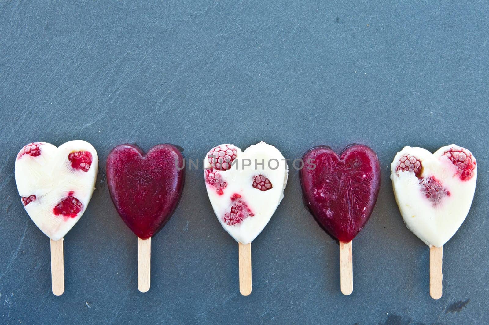 Ice cream on the stem in heart shape with fresh raspberries