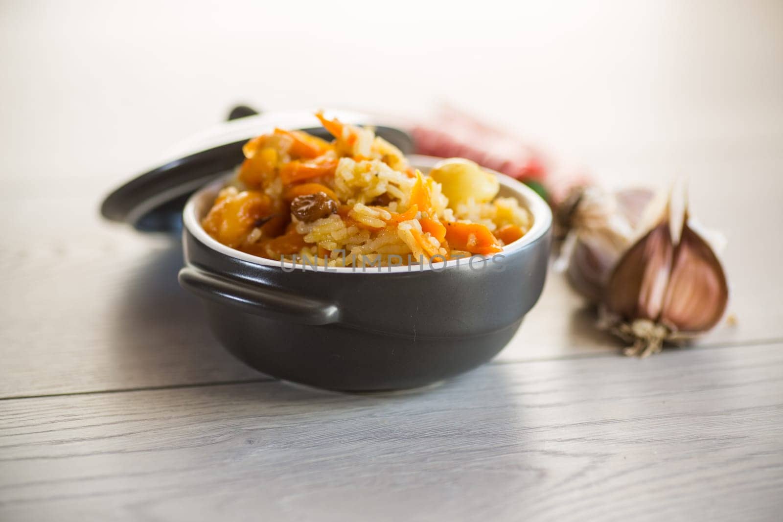 Cooked classic pilaf with meat, raisins, garlic and other ingredients in a bowl on a wooden table.