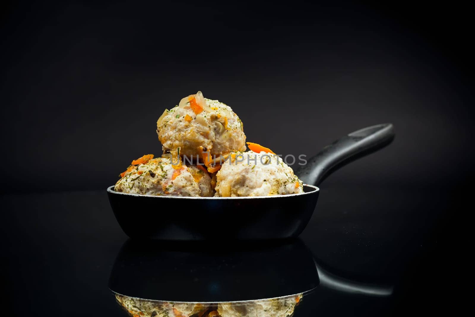 cooked chicken diet meatballs in a frying pan, isolated on a black background