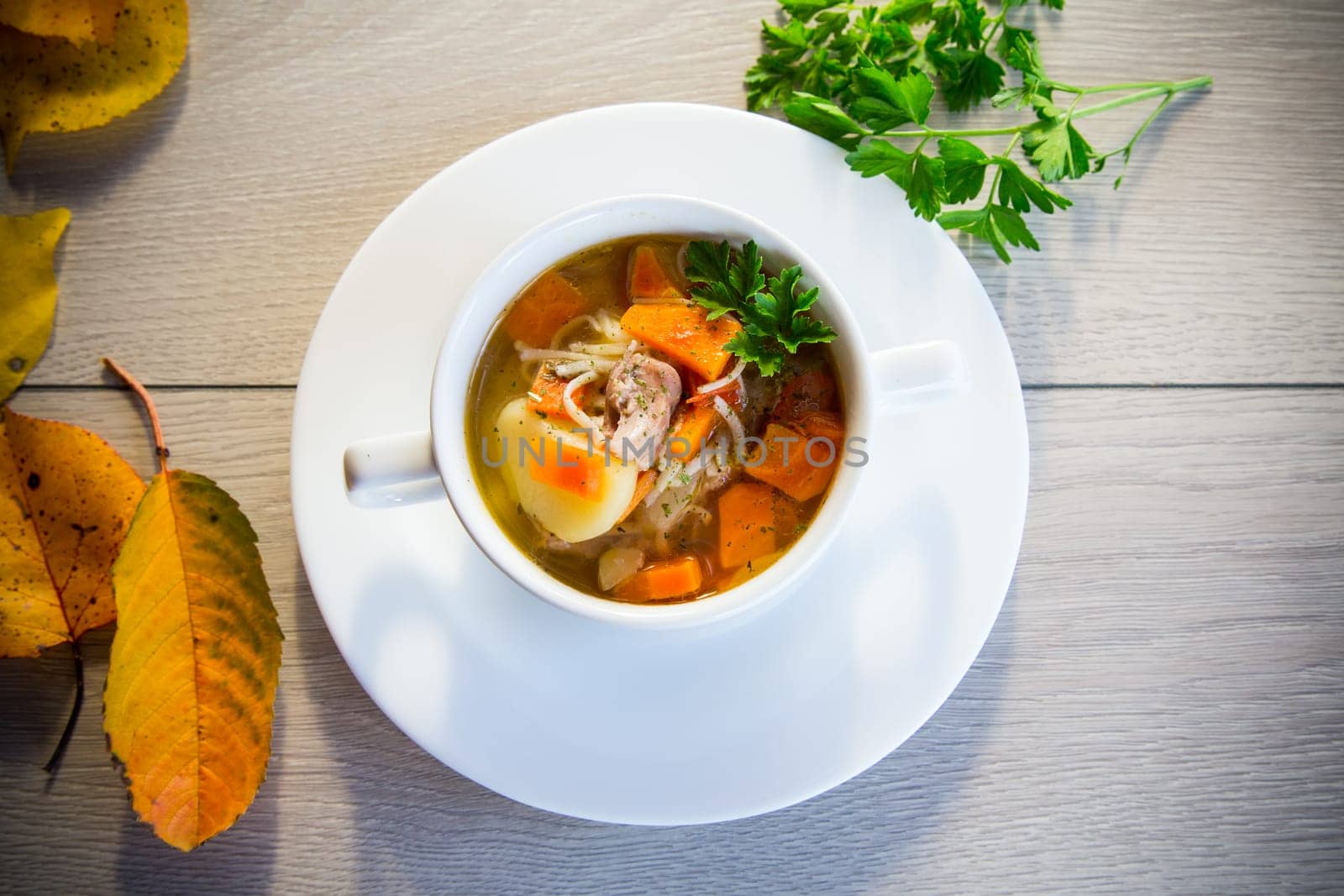 Autumn soup with chicken, noodles and autumn vegetables in a bowl on a wooden table.