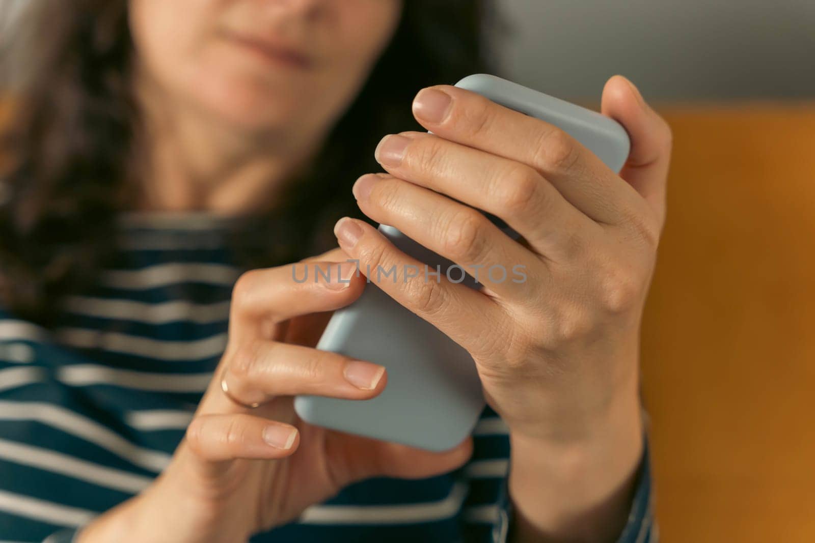 a girl in jeans and a striped blouse sits on the sofa and scrolls pages on the smartphone screen. digital communication in the modern world.