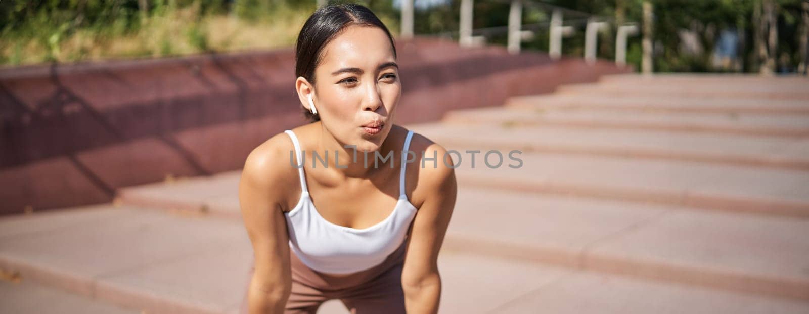 Portrait of sportswoman panting, taking break during jogging training, sweating while running outdoors.