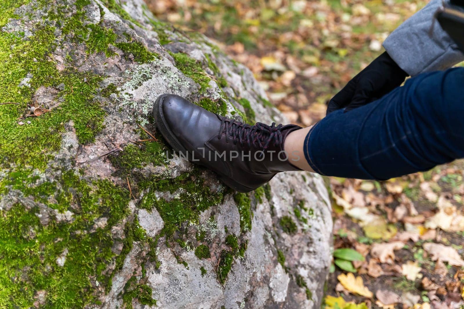 women's feet in leather autumn boots and jeans stand on a large boulder covered with green forest moss. Walking in the woods. Nature and active recreation