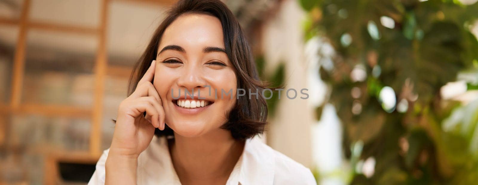 Close up portrait of funny young asian woman, sitting in cafe, chatting lively, smiling at camera.