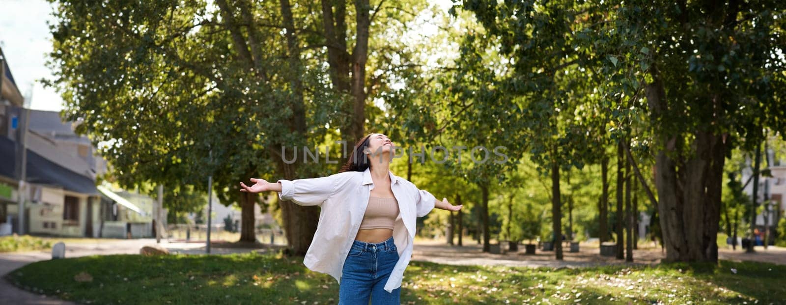 Carefree asian girl dancing, feeling happiness and joy, enjoying the sun on summer day, walking in park with green trees by Benzoix