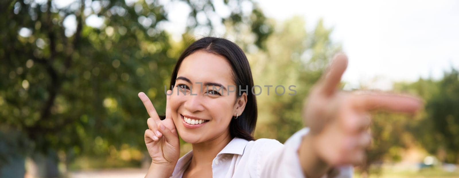 People and lifestyle. Happy asian woman takes selfie in park, photo on smartphone, smiling and looking joyful by Benzoix