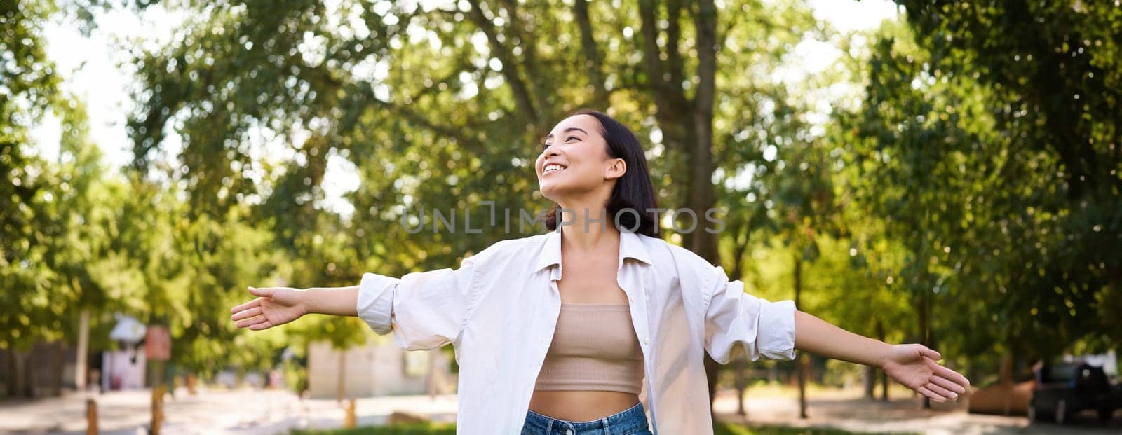 Portrait of carefree young asian woman dancing in park alone, enjoying freedom, smiling with joy by Benzoix