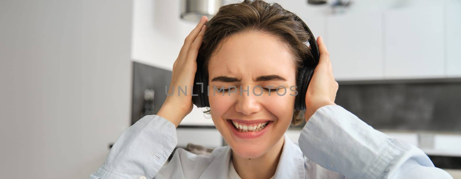 Close up portrait of woman, getting emotional from music, listening to song in wireless headphones, smiling and laughing.