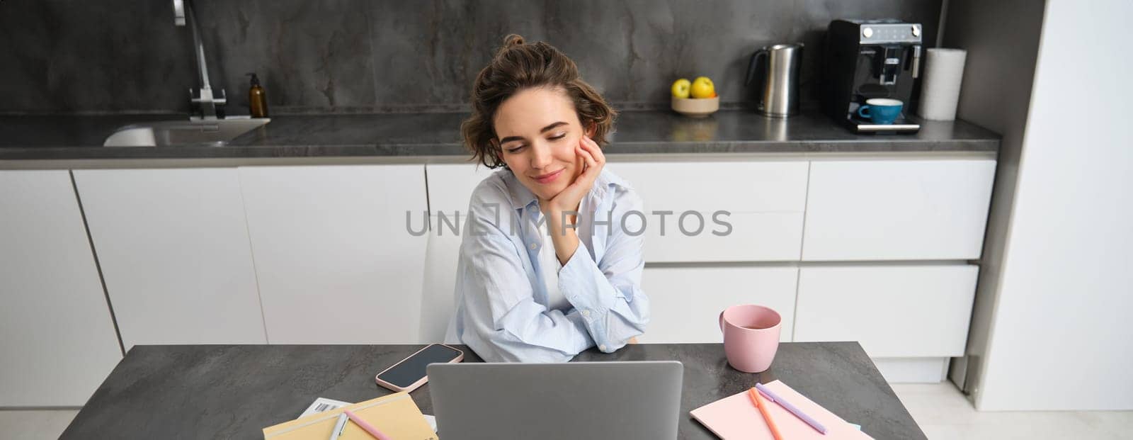 Image of young working woman, looking at laptop, sitting at home and watching webinar, connecting to team meeting, studying indoors.