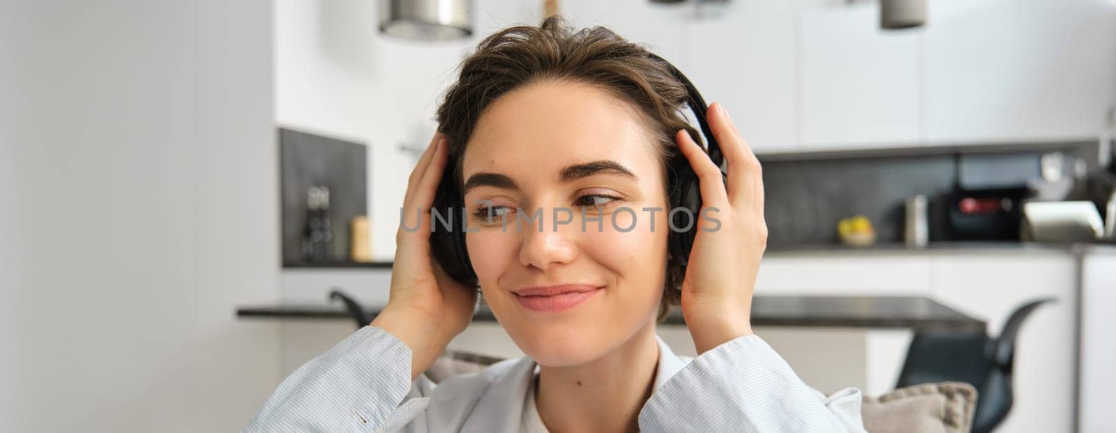 Close up portrait of happy, smiling girl, puts on wireless headphones, listens to music or e-book, sits at home on sofa. Copy space