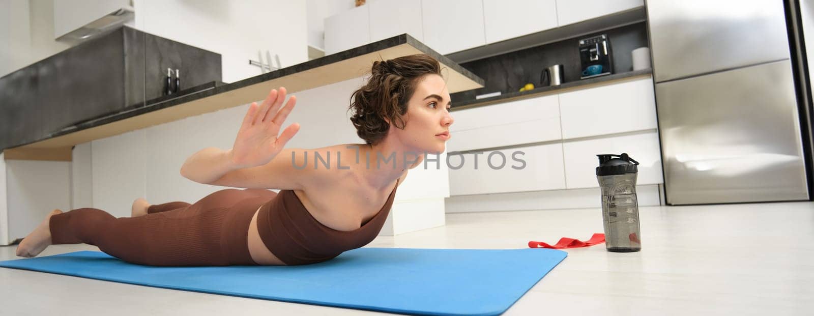 Portrait of sportswoman at home, doing workout training, stretching arms forward, leading active lifestyle from indoors, using resistance band and plunk push up bars for exercising.