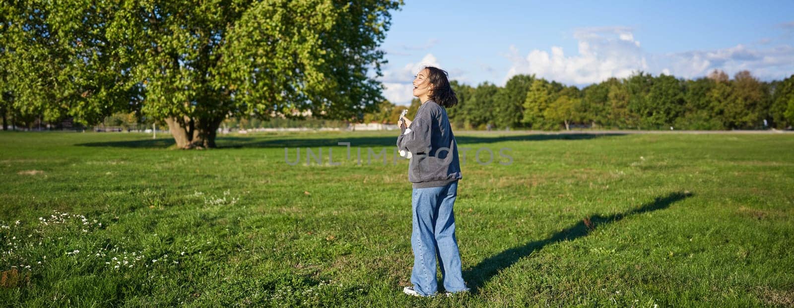 Happy young woman feeling carefree, walking in green park and playing ukulele, singing along by Benzoix