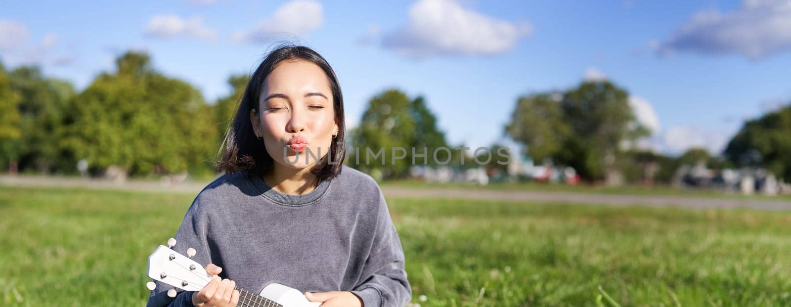 Positive hipster asian girl, playing ukulele and making faces, singing and feeling happy.