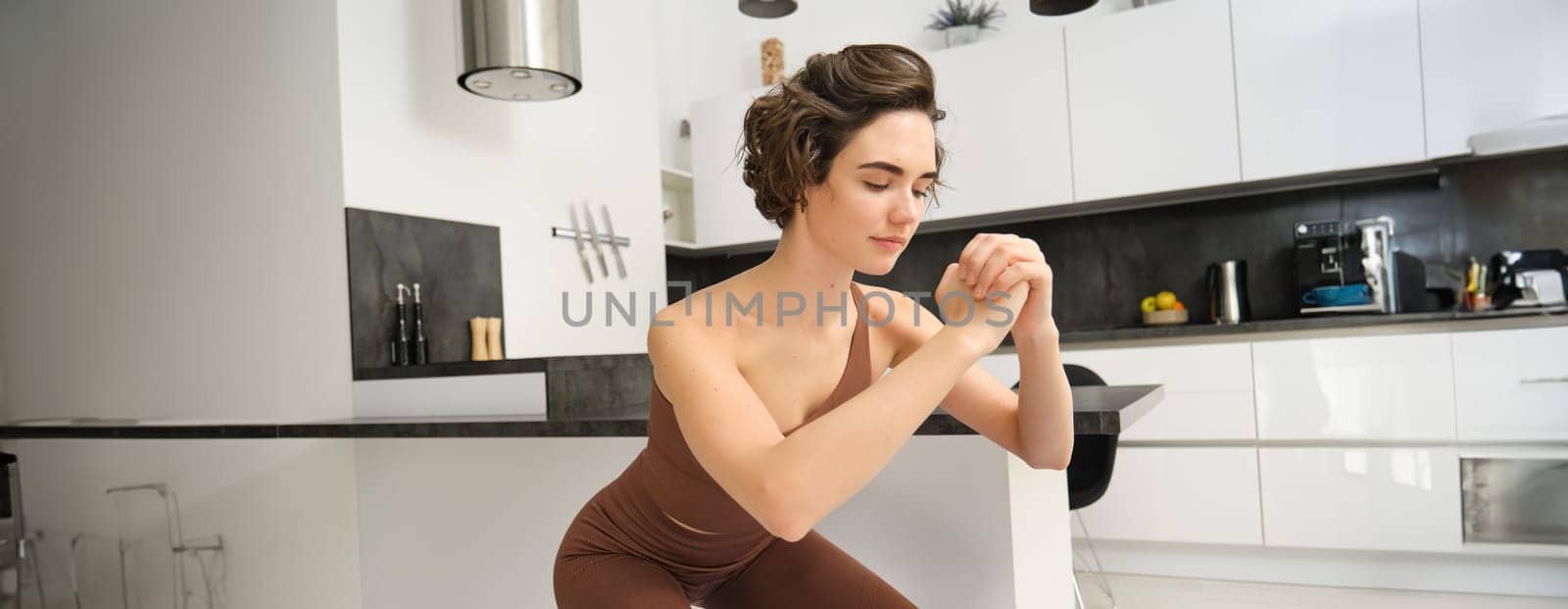 Workout and women wellbeing concept. Young fitness woman, doing squats, workout from home without gym equipment, training in bright room by Benzoix