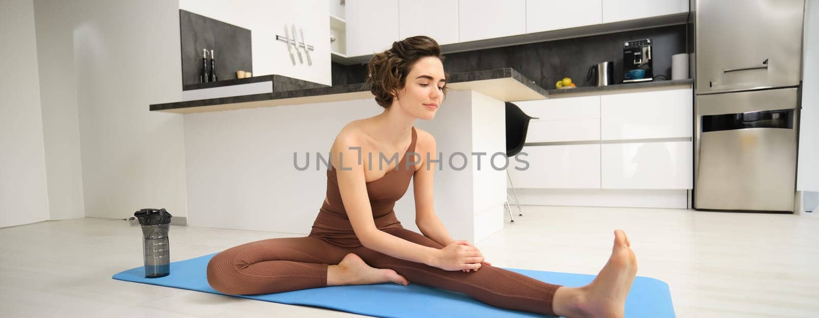 Image of brunette girl, stretching her legs, doing fitness workout, feet exercises to warm up before yoga, training at home alone.