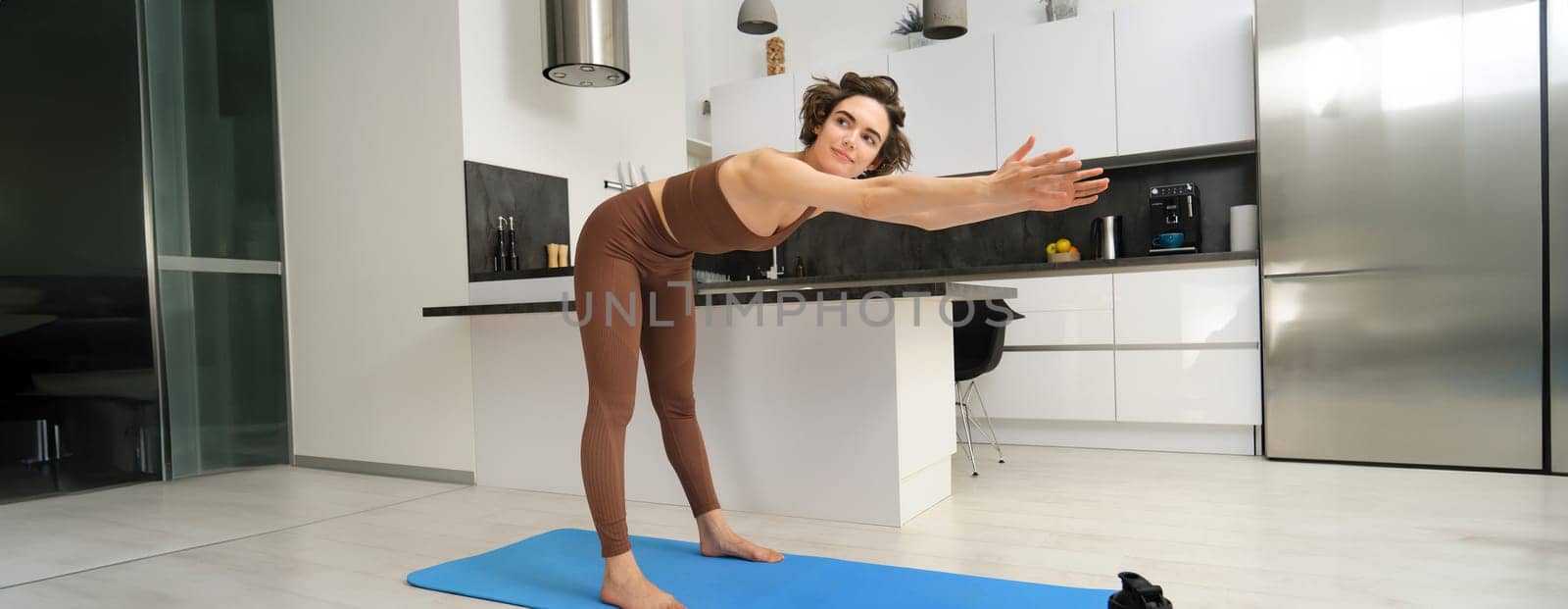 Woman follows gym video tutorial on smartphone while workout at home. Fitness girl does training at home on rubber yoga mat.
