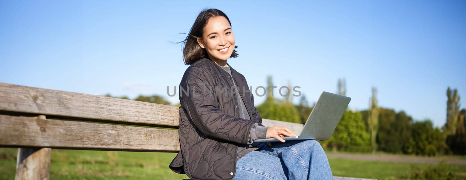 Digital nomad. Portrait of young woman using laptop in park, sitting on bench and working, studying online.
