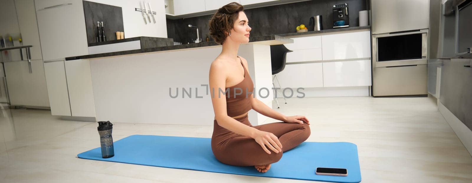 Fit healthy young woman doing pilates yoga exercise fitness training workout at home interior standing in warrior pose. Physical activity for body and mind relaxation, healthy lifestyle concept.