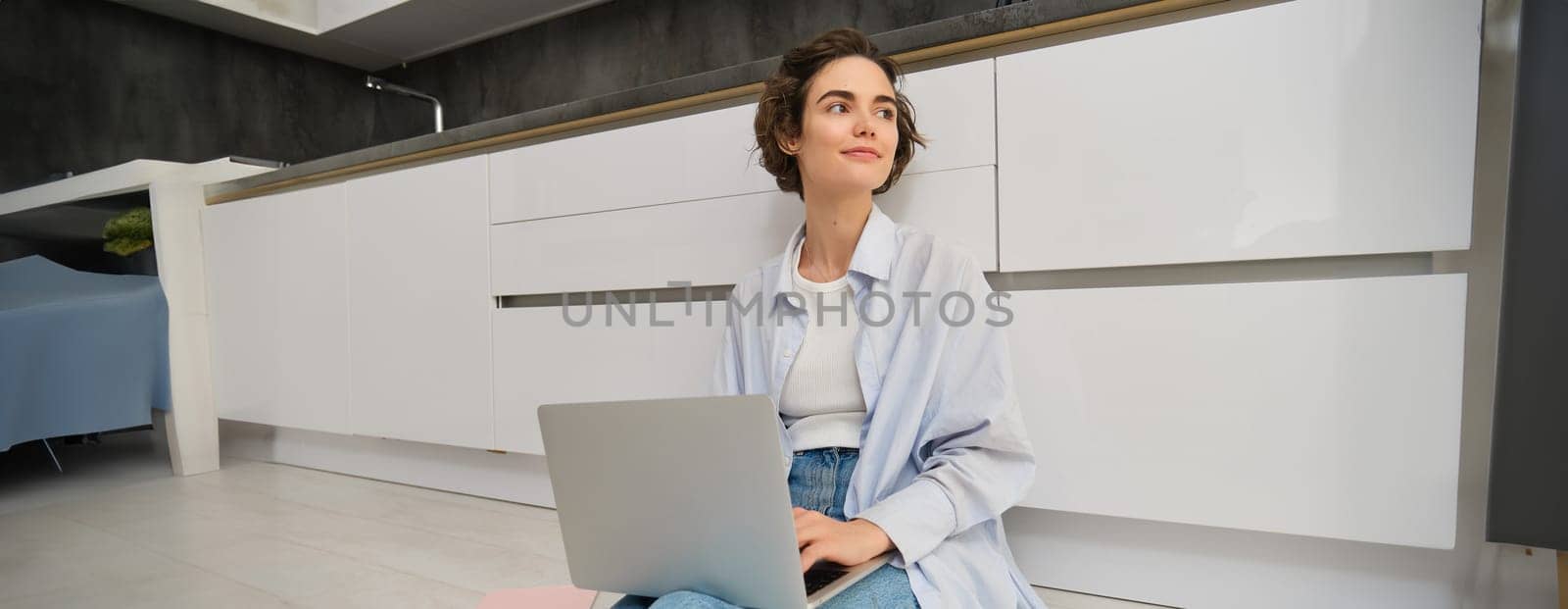 Young IT girl, woman works freelance from home, sits on floor with laptop. Girl student does homework online, writes on computer keyboard.