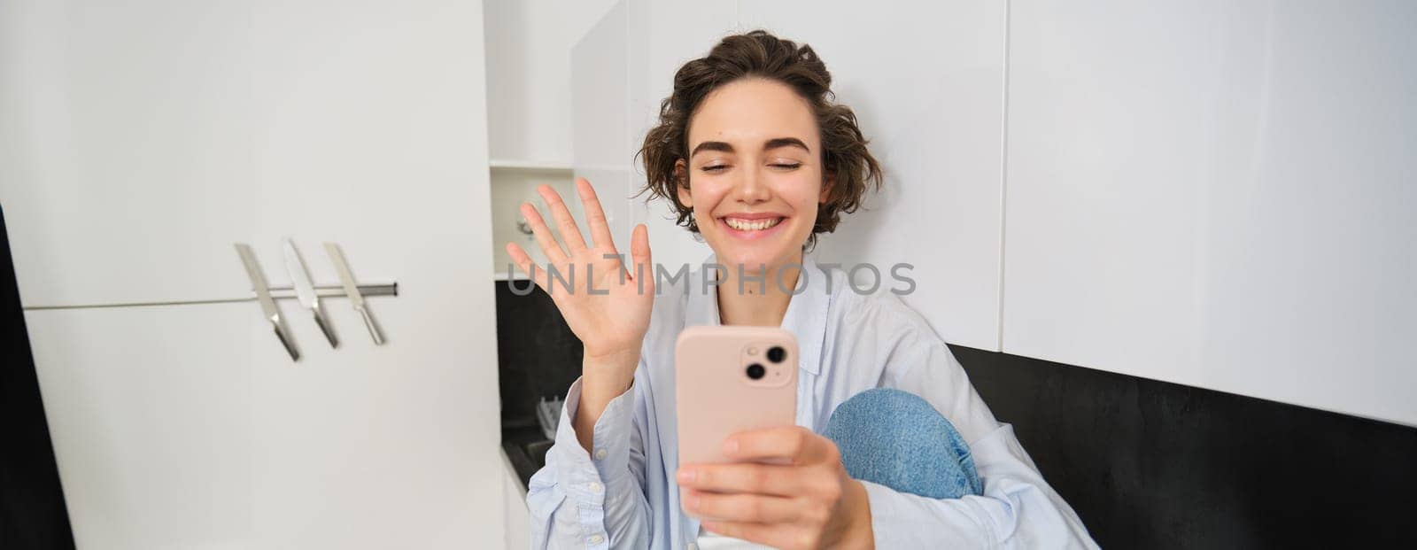 Happy smiling girl, saying hi to a friend on video chat, waves at smartphone app, connects to online conversation on her phone.