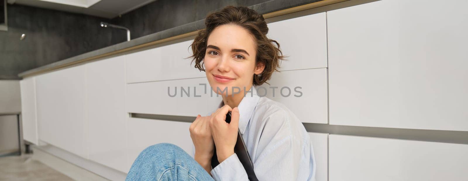 Image of happy young woman sits at home on floor, holds digital tablet, does online shopping, reading e-book. Copy space