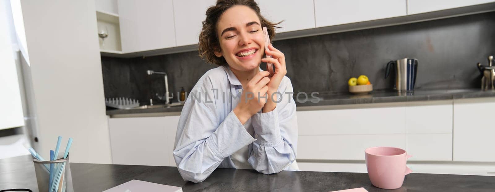 Portrait of cute smiling girl talks on mobile phone, sits at home and calls someone with smartphone.