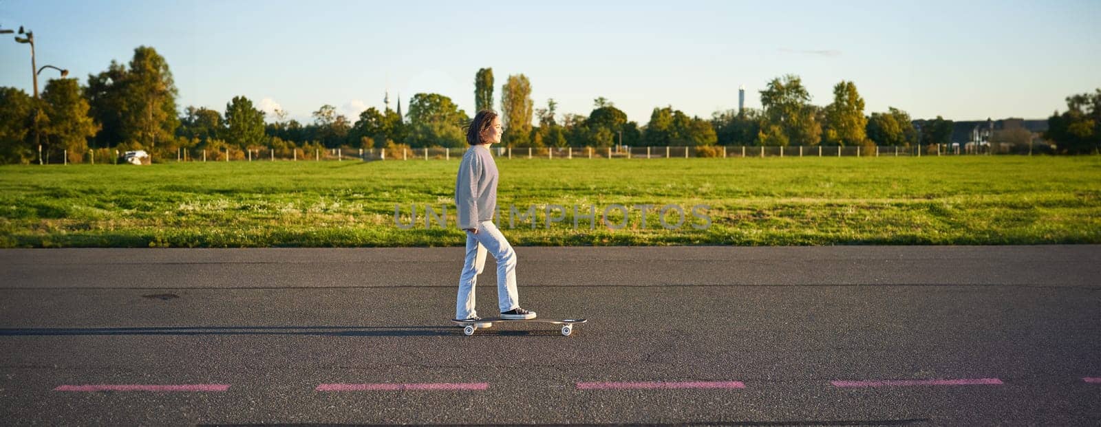 Beautiful asian skater girl riding her longboard on sunny empty road. Young woman enjoying her skate ride smiling and laughing.