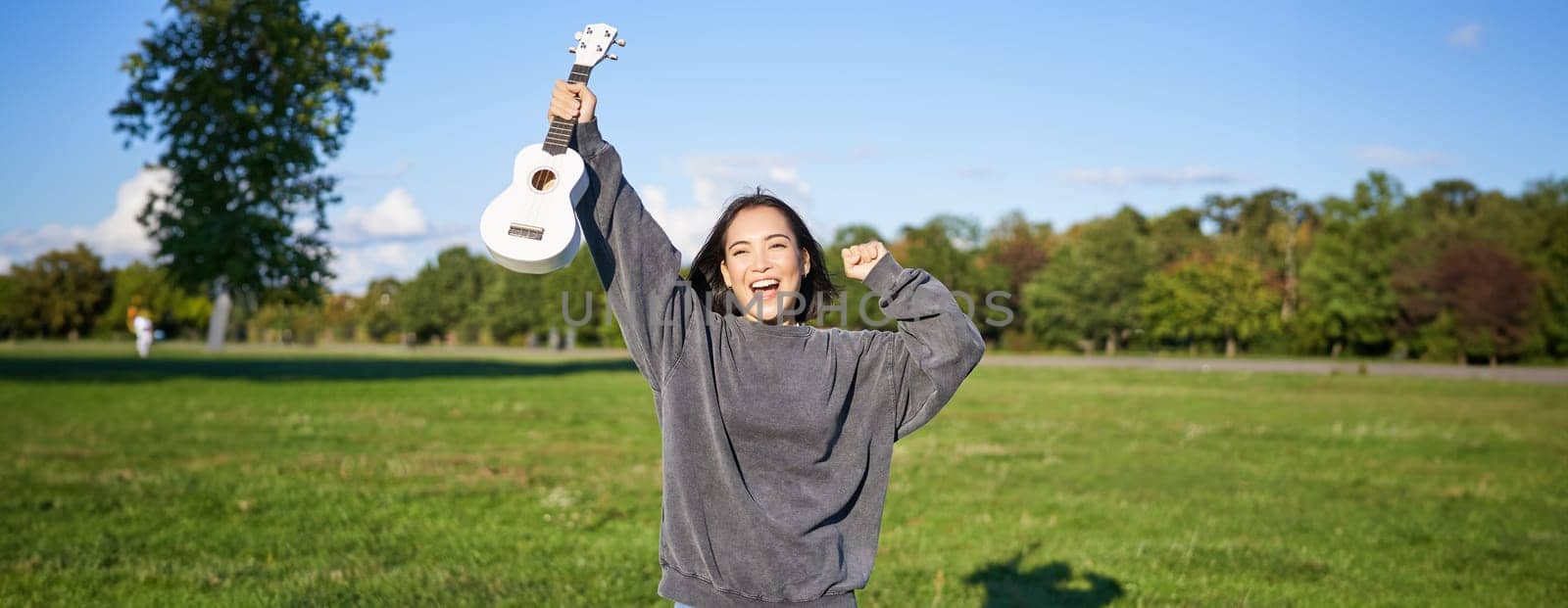 Positive beauty girl with ukulele, dancing and feeling freedom, looking excited, triumphing and celebrating.