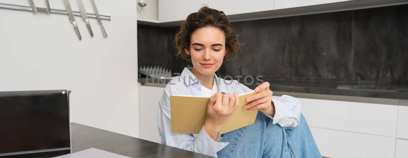 Portrait of modern girl, sits at home and reads through her notes, looks at journal, makes plans for week.