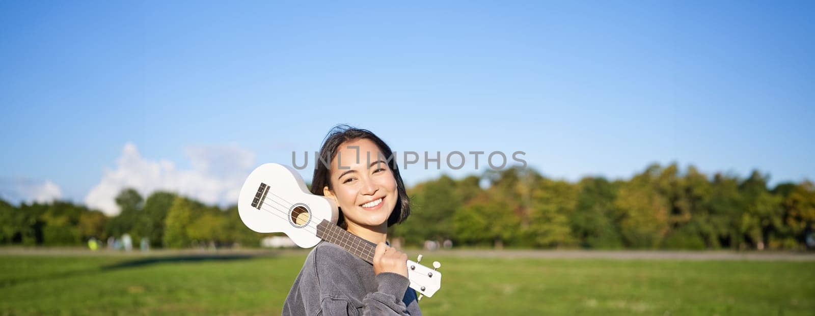 Young hipster girl, traveler holding her ukulele, playing outdoors in park and smiling. People concept