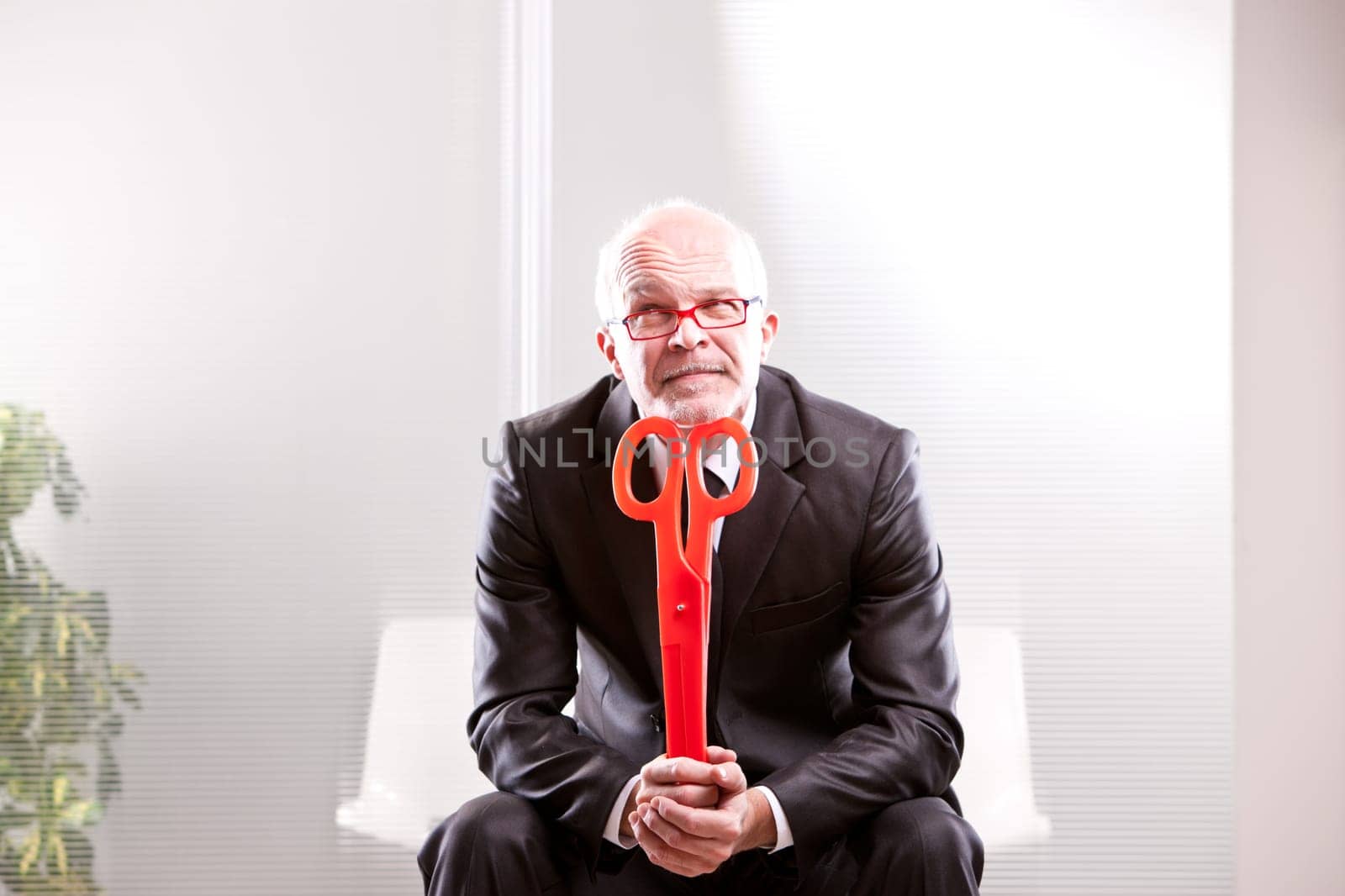 businessman thinking with a pair of red scissors in his hands