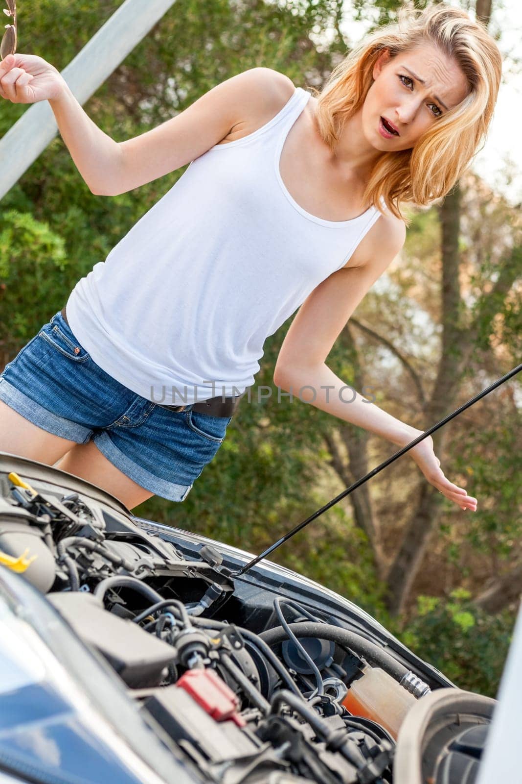 Attractive blonde woman on a road with a car breakdown and open engine compartment